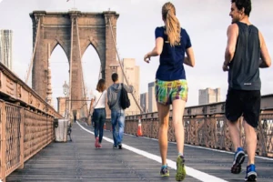 Young people jogging across Brooklyn Bridge, demonstrating active lifestyle and physical fitness that can be maintained at any age through the natural regenerative properties of deer velvet