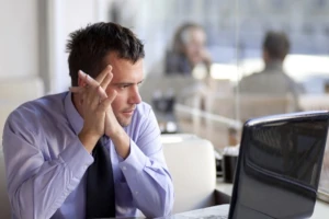 Tired man in office holding his head, illustrating mental exhaustion and energy depletion that can be alleviated by natural bioactive compounds from deer velvet